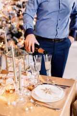 New Year 2020. New Year mood. Table with a gold tablecloth, decorated with candles and tableware for celebration. Festive still life by candlelight.A man pours champagne into a glass. Close-up.