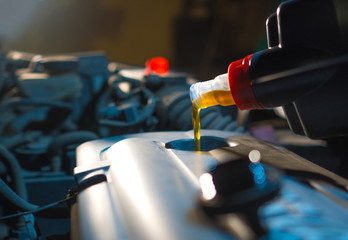 Engine oil change. Fresh engine oil pouring from the bottle into the automobile engine. Proper car care background.