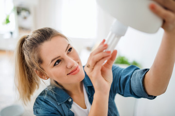 Young woman indoors at home, changing light bulb.