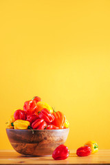 Colorful scotch bonnet chili peppers in wooden bowl over orange background. Copy space.