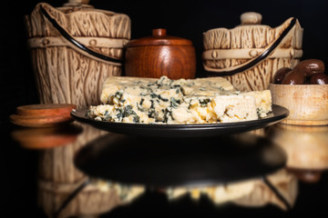 Blue cheese, small wooden bowl with olives and vintage bowls, with reflection on shiny black background