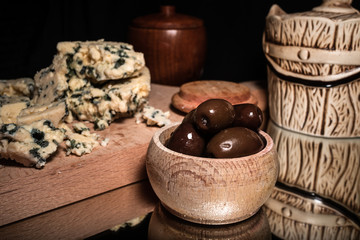 Blue cheese, small wooden bowl with olives and vintage bowls, with reflection on shiny black background