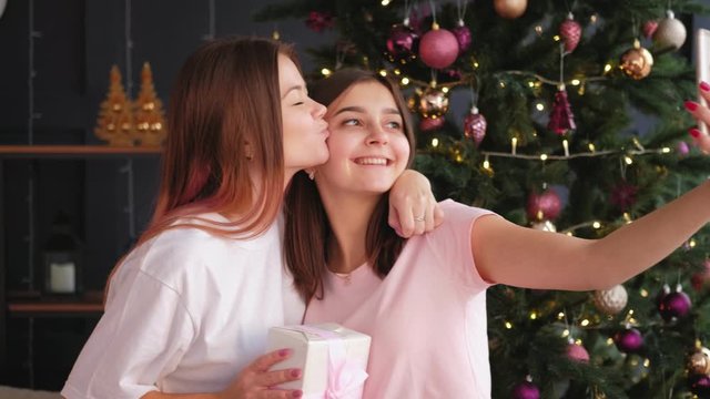 Festive photoshoot. New Year party. Two happy sisters posing on smartphone camera with gift box.