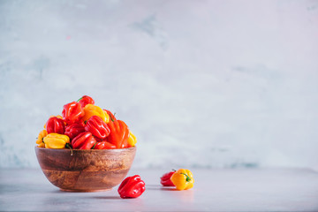 Colorful scotch bonnet chili peppers in wooden bowl over grey background. Copy space.