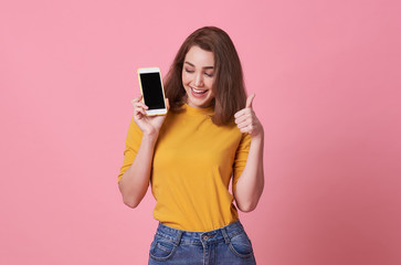 Naklejka premium Portrait of happy young woman showing at blank screen mobile phone and hand gesture good isolated over pink background.