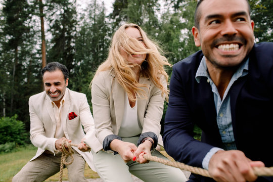 Smiling male and female colleagues pulling rope while playing tug-of-war