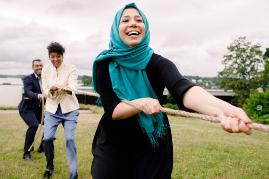 Smiling multi-ethnic male and female colleagues pulling rope while playing tug-of-war in lawn