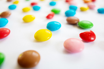 Scattered multi-colored small round candies. Chocolate dragees in multi-colored glaze on a white background.