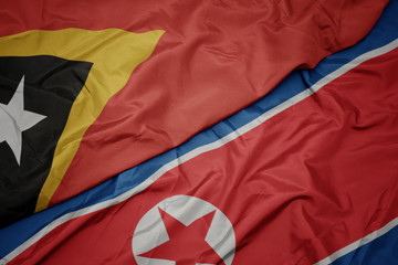 waving colorful flag of north korea and national flag of east timor.