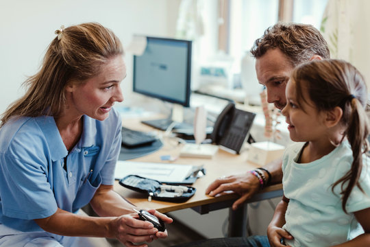Smiling girl looking at doctor showing glaucometer in medical examination room