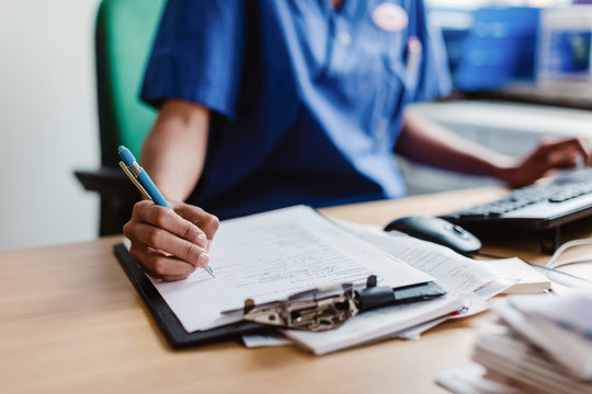Midsection of nurse writing medical report while sitting at desk in clinic
