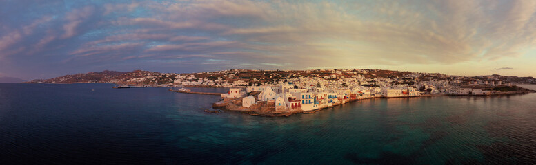 Aerial drone panoramic photo of picturesque old port in main village of Mykonos island at sunset and iconic church of Paraportiani with beautiful colours, Cyclades, Greece