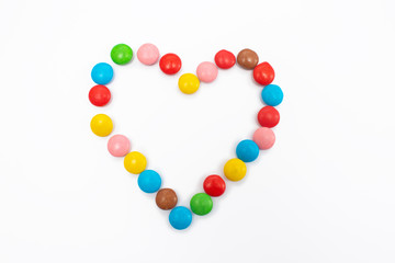 Multicolored round jelly beans collected in the form of a heart on a white background.
