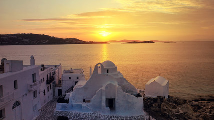 Aerial drone panoramic view of landmark church of Paraportiani overlooking the Aegean sea in main village of Mykonos island at sunset with beautiful colours, Cyclades, Greece - obrazy, fototapety, plakaty