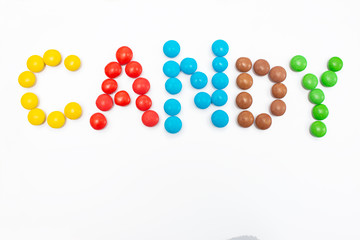 The inscription Candy written in round small multi-colored sweets dragees on a white background