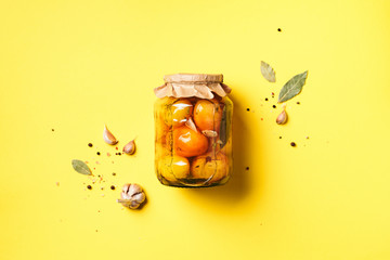 Pickled tomatoes in jar on yellow background. Top view. Flat lay. Copy space. Canned and preserved vegetables. Ingredients for vegetables preserving. Healthy fermented food concept.