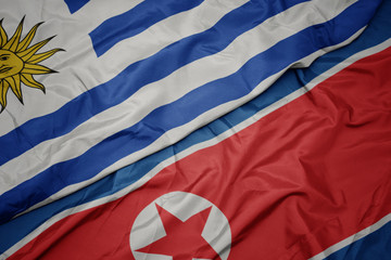 waving colorful flag of north korea and national flag of uruguay.