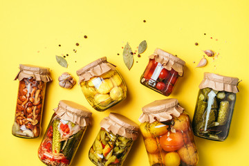 Fototapeta na wymiar Canned and preserved vegetables in glass jars over yellow background. Top view. Flat lay. Copy space.