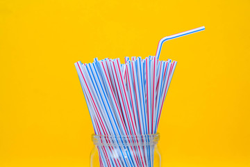 Plastic straws in a glass jar with yellow background. Space for text