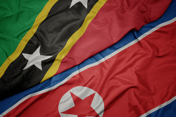 waving colorful flag of north korea and national flag of saint kitts and nevis.