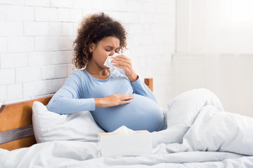 Pregnancy and illness. Sick woman blowing nose in tissue