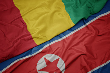 waving colorful flag of north korea and national flag of guinea.