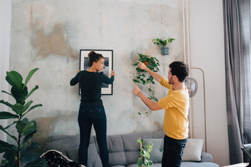 Boyfriend guiding girlfriend in hanging picture frame on wall at new home