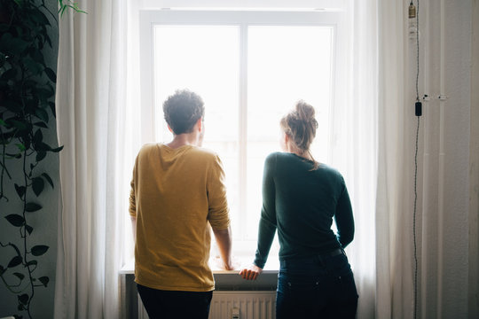 Rear view of couple looking through window while standing at home
