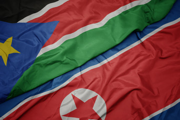 waving colorful flag of north korea and national flag of south sudan.