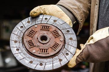 Auto mechanic in protective work gloves, holds used clutch disc. Clutch disc friction pad....