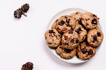 Christmas cherry, chocolate and pecans oatmeal cookies on grey  background decorated fir cones. Selective focus