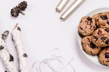 Christmas cherry, chocolate and pecans oatmeal cookies on grey  background decorated fir cones, birch branches and candles. Hygge. Selective focus