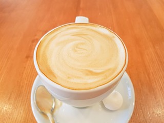 Cappuccino in a white cup on the wooden table. Closeup and top view.