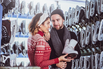 Young couple standing near rack with many pairs of skates, choosing his size