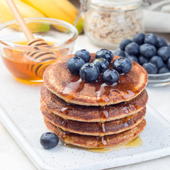 Healthy oatmeal banana pancakes garnished with blueberry and honey, on  white board,  square format