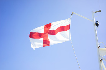English flag on a flagpole on a boat against a blue sky with soft clouds in the summer