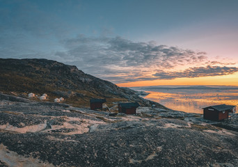 Naklejka premium Panoramic image of Camp Eqi at Eqip Sermia Glacier in Greenland. nature landscape with lodge cabins. Midnight sun and pink sky. Tourist destination Eqi glacier in West Greenland AKA Ilulissat and