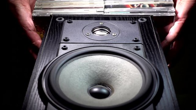 POV shot from below of a man&rsquo;s hands placing CDs on top of a wood grained speaker cabinet, to form a convenient shelf.