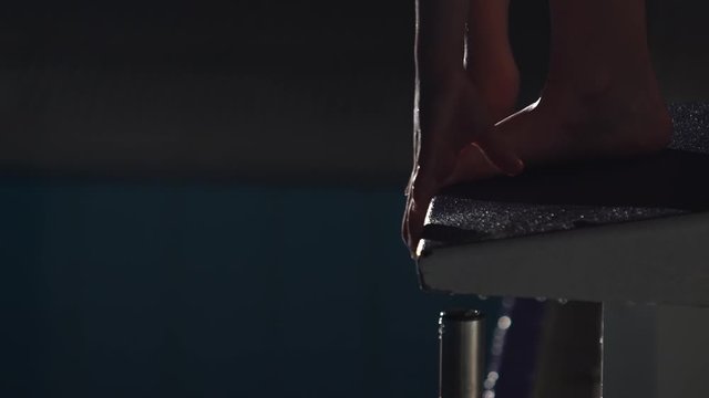 Close up shot in slow motion of a professional female swimmer's feet preparing to jump off the starting block into the swimming pool. Night shot