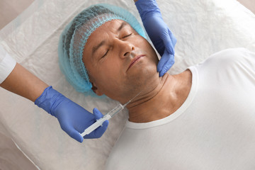 Mature man with double chin receiving injection in clinic, above view