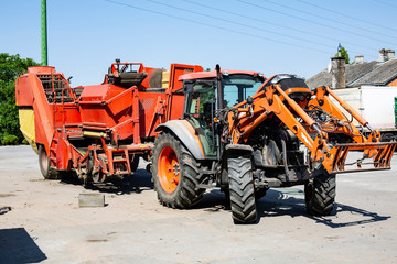 Red farm tractor with a potato harvester. Agricultural business. Machinery on a country farm on a...