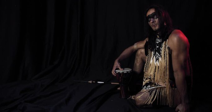 Native american man with long hair, wearing traditional clothes, touching a drum