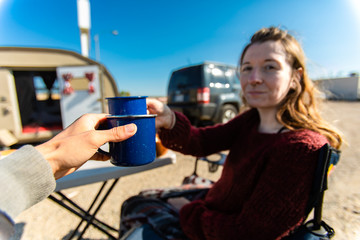 Selective focus of two adult persons drinking a cup of coffee or tea while sitting outside in front of their caravan camper