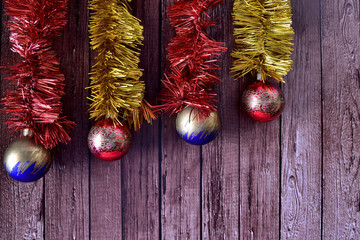 Christmas background, metallic garlands with decorated balls, on wooden background in slats. Red, blue, green and gold colors. Front view, space to write.