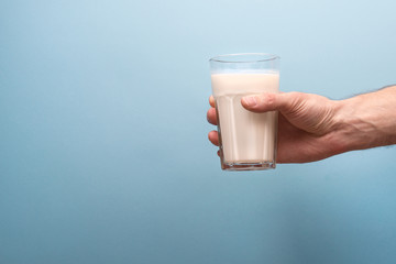 A glass of milk in a man’s hand on a blue background. Male hand holds a glass of milk. Milk on a...