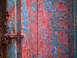 Vintage wooden door with flaking blue paint, locked with a rusty tab and a padlock.