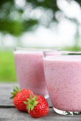 A glass of fresh cold smoothie with berries and cherrys on a wooden table, summer set, outdoor greed blured background,boke.