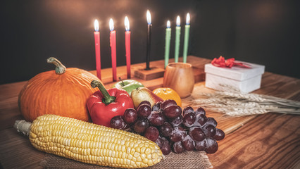 Kwanzaa holiday concept with decorate seven candles red, black and green, gift box, pumpkin,corn and fruit on wooden desk and background.
