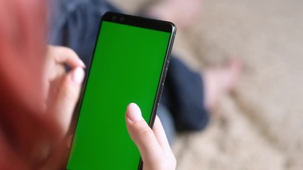 adult girl holding a phone with a green screen. Chromakey on the smartphone. Use the green layout to insert images. People use the chroma key online. Hand and finger gestures. Close up.