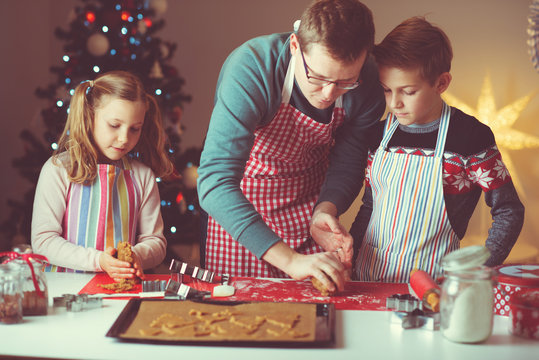 Happy father with his children bakes ginger cookies for Christmas with christmas tree on background
